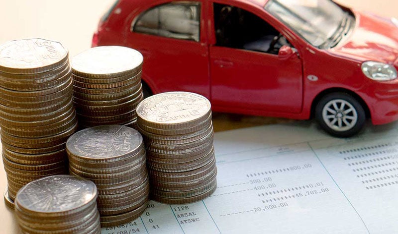 A stack of coins in front of a red car